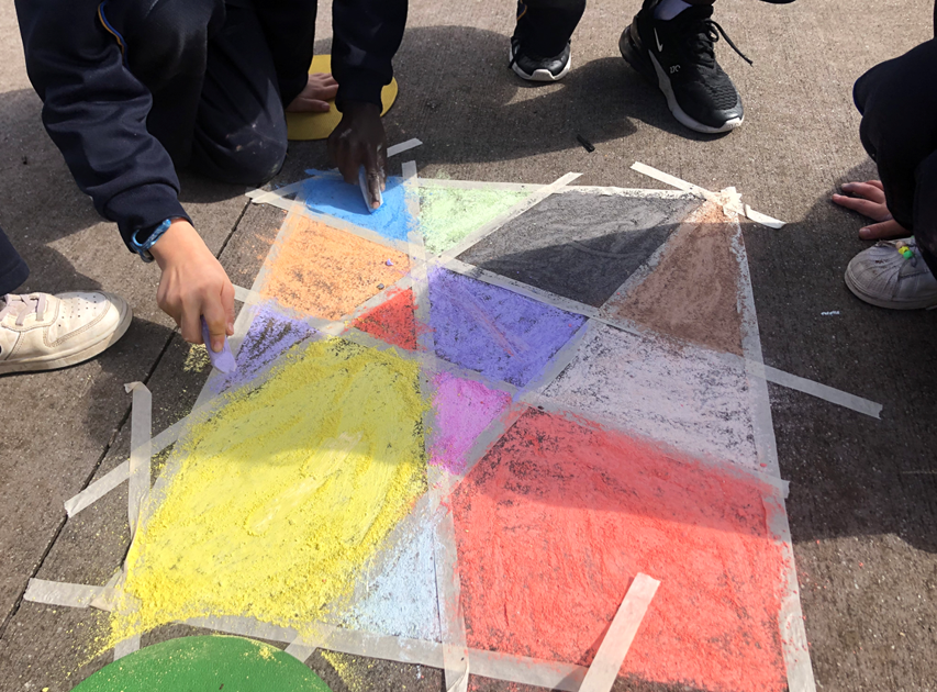 A group of people drawing on the ground to make angular coloured shapes like a stain glass window