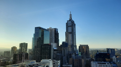 City skyline view showing a number of buildings increasing in size to a central skyscraper with a tall spire, all surrounded by blue sky.